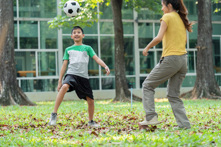 Fun and Bonding Through Soccer. A young boy joyfully plays soccer in the park with his mom.の写真素材
