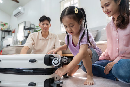 Childhood Discovery and Family Interaction. A little girl plays with a suitcase beside her parents.の写真素材