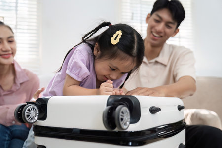 Playful Exploration and Family Fun. A little girl engaged with her suitcase while her parents cheer her on.の写真素材