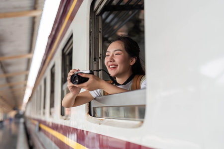 Photography and Travel. A joyful woman capturing memories as she leans out of a train window, enjoying the journey.の写真素材