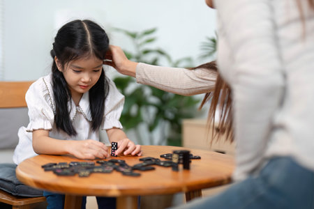 Engaging Learning Moments in Family Activities. A girl deeply focused on her game pieces, supported by her mother.の写真素材