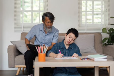Creative Engagement and Family Support. A grandfather observing a child drawing with colored markers.の写真素材