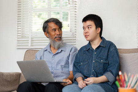 Family Bonding and Technology. A caring grandfather and his grandchild engaging in a meaningful conversation while using a laptop.の写真素材