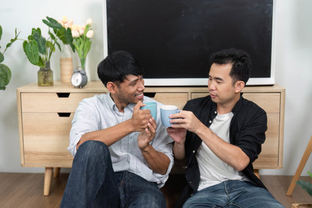 Friendship and Coffee Moments. Two men toasting with coffee mugs in a relaxed living room.の写真素材