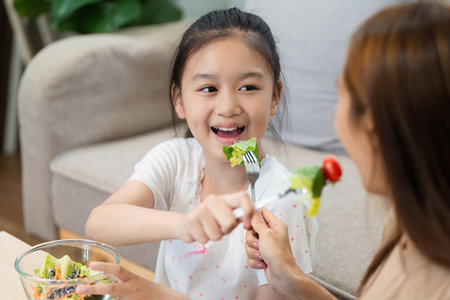Wellness through sharing: Girl feeding salad to her motherの写真素材