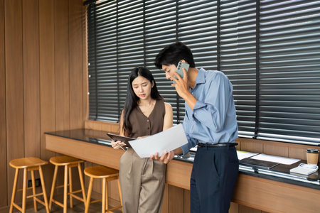 Business Collaboration and Analysis. Two professionals reviewing project documents in a contemporary office.の写真素材