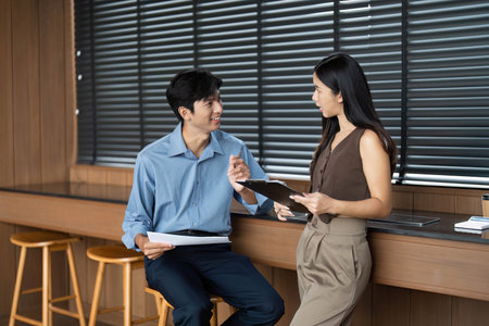Business Collaboration and Communication. Two professionals discussing project details in a modern office.の写真素材