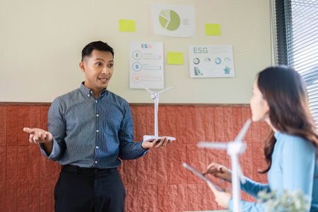 ESG Presentation on Renewable Energy. Professional explaining wind turbine model to colleague.の写真素材