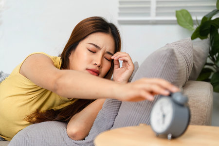 Morning Routine and Waking Up. A woman groggily reaching for an alarm clock to turn it off and start...