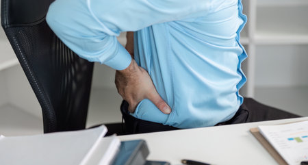 Young Businessman Experiencing Back Pain While Working in a Modern Office Environmentの写真素材