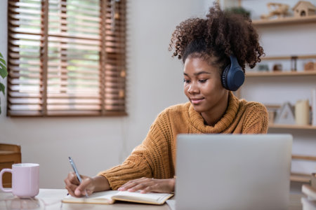Young African Woman Working Online from Home, Relaxing with Laptop and Headphones in Cozy Living...