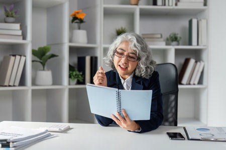Elderly businesswoman reviewing notes and strategizing in a modern workspace, showcasing leadership...