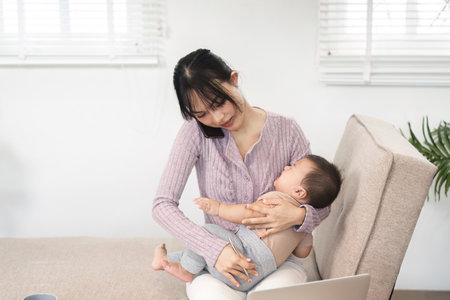 Single mom balancing work and parenting while discussing tasks on the phone with her baby in her lapの写真素材