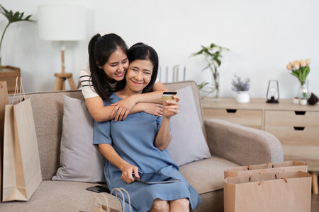 Two joyful women happily embracing while shopping online with a tablet and credit card at homeの写真素材
