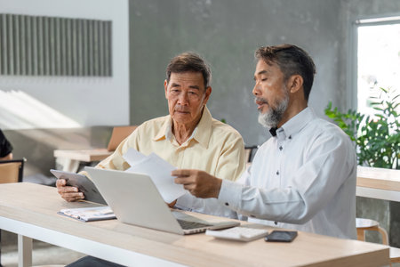 Experienced businessmen analyzing reports and discussing strategy in a contemporary office spaceの写真素材