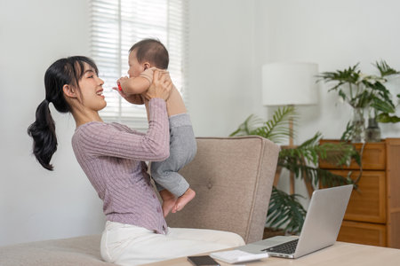 Joyful mother lifting her baby in the air, celebrating love and connection during work from homeの写真素材