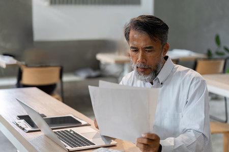 Male businessman reviewing important documents while working in a modern office settingの写真素材