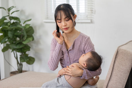 Busy mother multitasking on a phone call while nurturing her baby at home