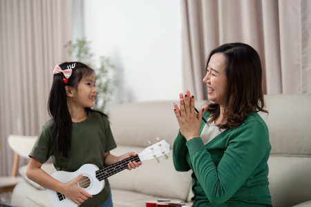 Joyful Music Moment. Young girl playing ukulele while mother celebrates her performance.の写真素材