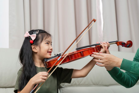 Music Education and Bonding. Young girl learning violin from her mother at home.の写真素材
