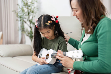 Music Education and Bonding. Mother teaching daughter to play ukulele at home.の写真素材