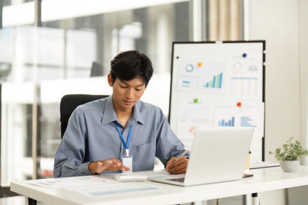 Productive Workspace. Young man using smartphone while working on laptop.の写真素材