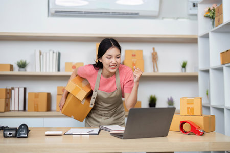Small Business Success. Young entrepreneur celebrating order fulfillment in a home office.の写真素材
