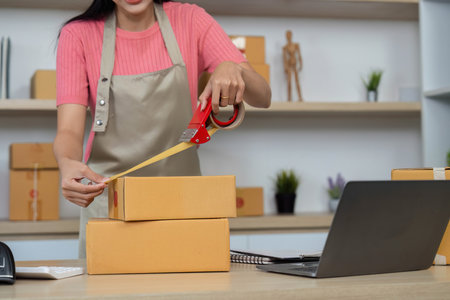Small Business Shipping. Female entrepreneur packaging orders with tape in a retail workspace.の写真素材
