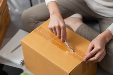 Moving tasks. Woman using a utility knife to open a delivery box.の写真素材