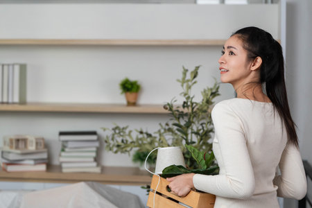 Moving and Unpacking. Woman smiling while carrying a crate with plants indoors.の写真素材