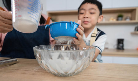 Family Cooking Moments. A boy learning to measure ingredients with his mother in the kitchen.の写真素材