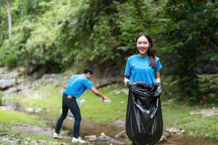 Volunteer teamwork. Young woman and man cleaning up a stream.の写真素材