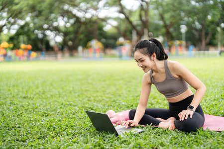Yoga and Digital Wellness. Smiling woman using laptop while practicing yoga outdoors.の写真素材