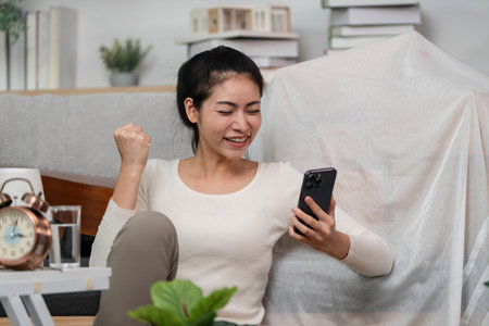 Moving excitement. Young woman celebrating delivery while checking her smartphone.の写真素材