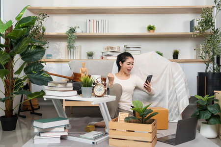 Moving and Celebrating. Woman excitedly using her smartphone while unpacking.
