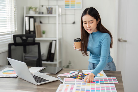 Productivity and Color Analysis. A designer assesses color samples while enjoying her coffee in a stylish workspace.の写真素材