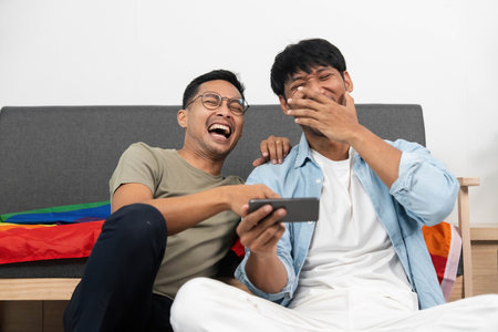 LGBTQIA Couple Sharing Laughter. Two young men enjoying a funny moment while watching something on their phone.の写真素材