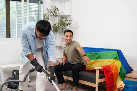 Home Cleaning and Inclusion. Friends vacuuming in a vibrant living space adorned with a rainbow flag.の写真素材