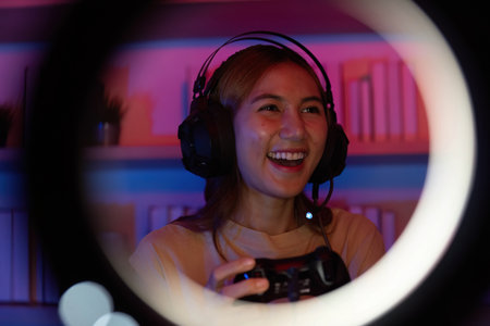 Excited Gamer in Action. Young woman enjoying gaming with a controller and vibrant lighting.の写真素材