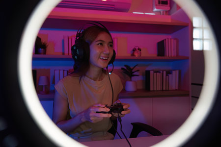 Gaming and Digital Entertainment. Young woman enjoying video game in colorful room with headphones.の写真素材