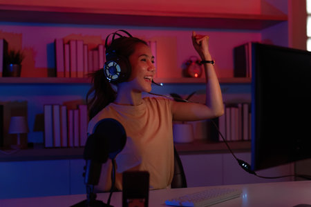 Victorious Gamer. Young woman celebrating her gaming success with a headset in a stylish...