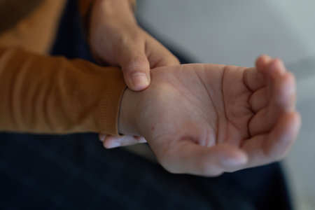 Health Awareness: Young woman checking wrist for discomfort at homeの写真素材