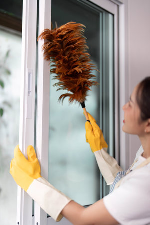 Home Cleaning. Woman dusting window with duster in modern interior.