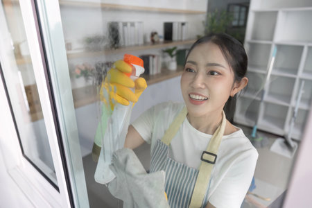 Home Cleaning. Young woman cleaning windows with spray and cloth, showcasing a bright and tidy...