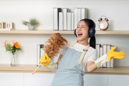 Happy Cleaning. Young woman smiling while holding a feather duster and headphones.