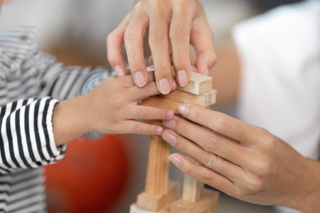 Family Bonding. Caregiver helping toddler build a wooden block tower, enhancing fine motor skills.の写真素材