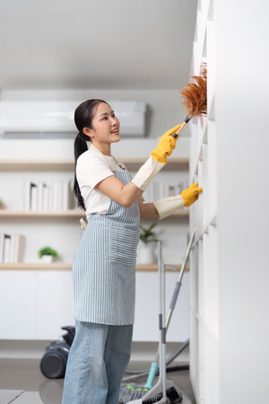 Home Cleaning. Young woman dusting shelves with a cheerful expression.