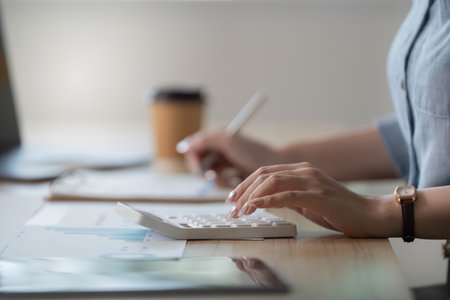 Remote Work. Woman calculating data with calculator at home office.の写真素材