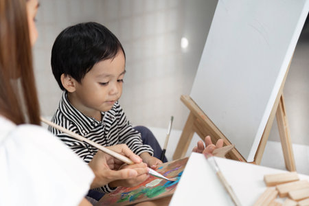 Child Concentrating on Painting with Motherâs Helpの写真素材