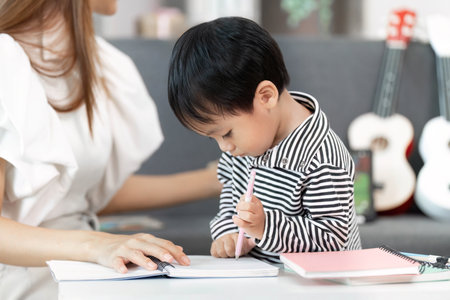Young Boy Concentrating on Drawing with Motherâs Guidanceの写真素材